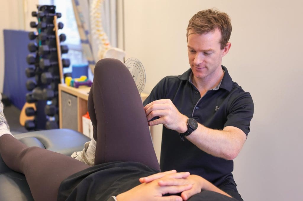 Physiotherapist assessing a client’s knee and hip mobility during a treatment session in clinic