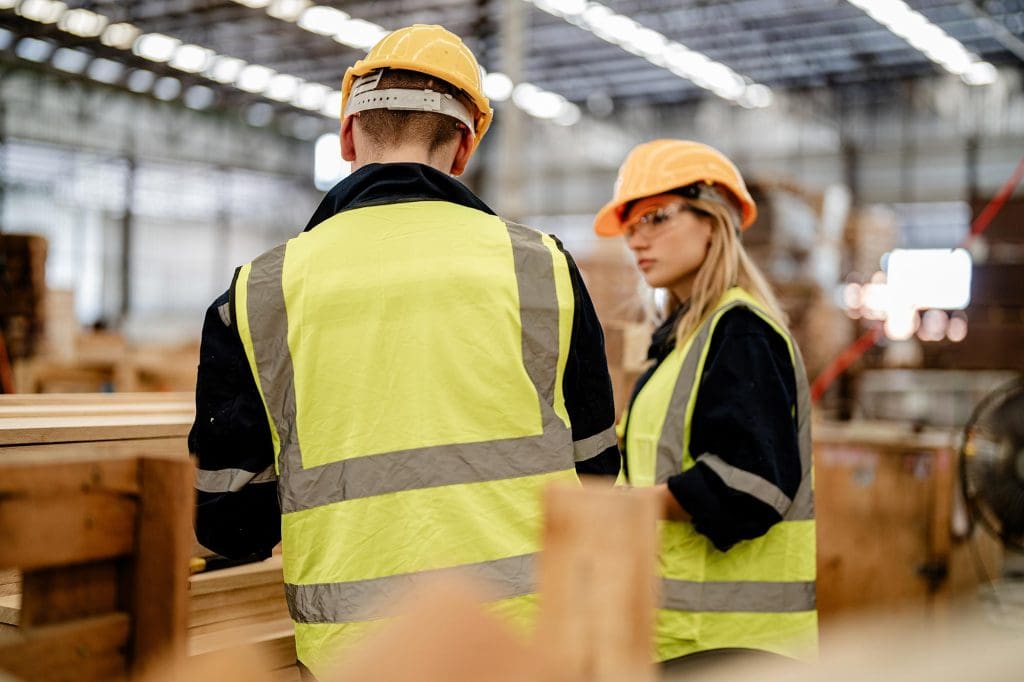 Woman worker in safety uniform and protective gear using a carpenter’s tool on a worksite