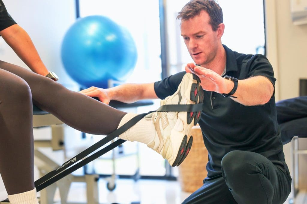 Physiotherapist guiding a patient’s leg exercise using a resistance band in a clinical rehab setting
