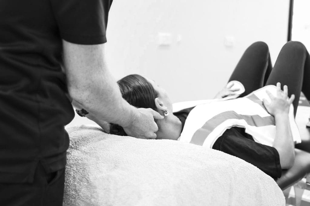 Physiotherapist’s hands gently supporting and adjusting a client’s neck while they lie on a treatment table during a physiotherapy session at a clinic